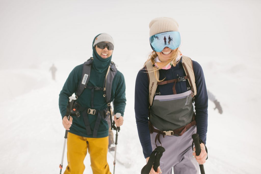 A male and a female skier wearing ski bibs on a white and snowy day