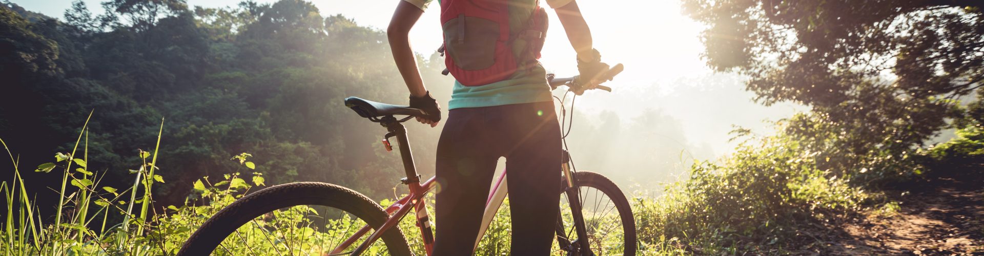 Young woman mountain biker enjoys the beautiful sunrise on summer forest trail