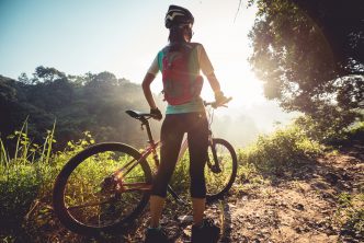 Young woman mountain biker enjoys the beautiful sunrise on summer forest trail