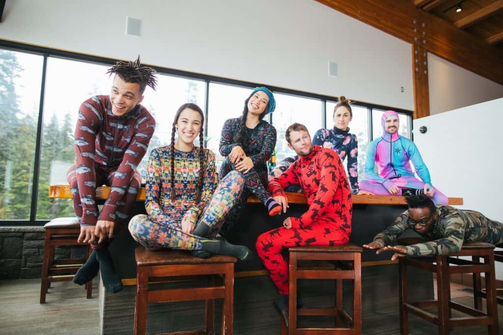 A group of smiling, happy, young skiers dressed in colorful base layers in a ski lodge