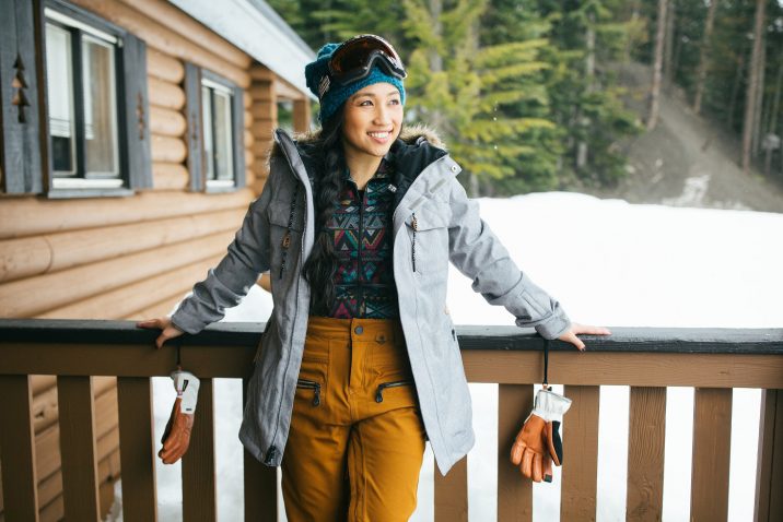 A young female skier wearing colorful gear standing on a covered porch in the snow