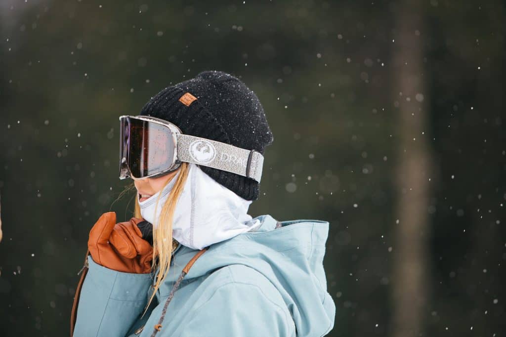 A young female skier with snow falling wearing ski goggles, ski jacket, gloves and a hat