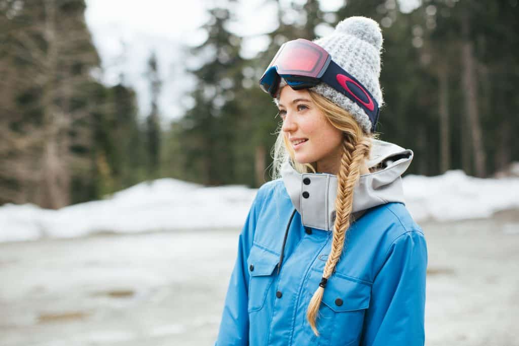 A young female skier wearing a blue jacket, a hat and ski goggles