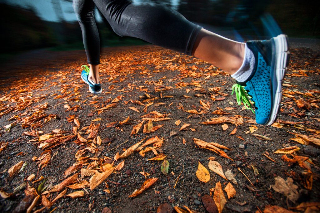 young woman trail running in the early evening autumn leaves